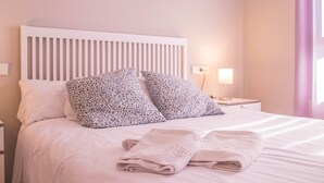 Una cama bien hecha con almohadas de estampado floral, un cabecero blanco y una lámpara de noche.