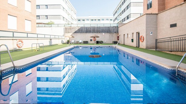 Ein Schwimmbad, umgeben von modernen Gebäuden, mit blauem Himmel.