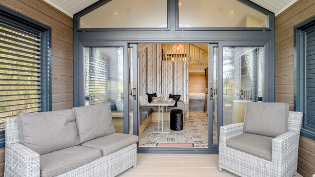 Ein modernes Interieur mit zwei grauen Sofas, einem Esstisch und einem durch Glastüren einsehbarer Küchenbereich.