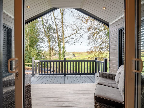 Um deck coberto com guarda-corpo, um sofá de vime e vista para árvores e um edifício ao longe.