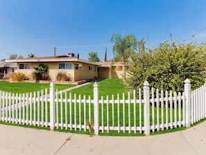 A single-story house with a white picket fence, a well-maintained lawn, and a clear blue sky.