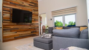 Een moderne woonkamer met een houten wandpaneel, een grijze bank en een flatscreen televisie aan de muur.