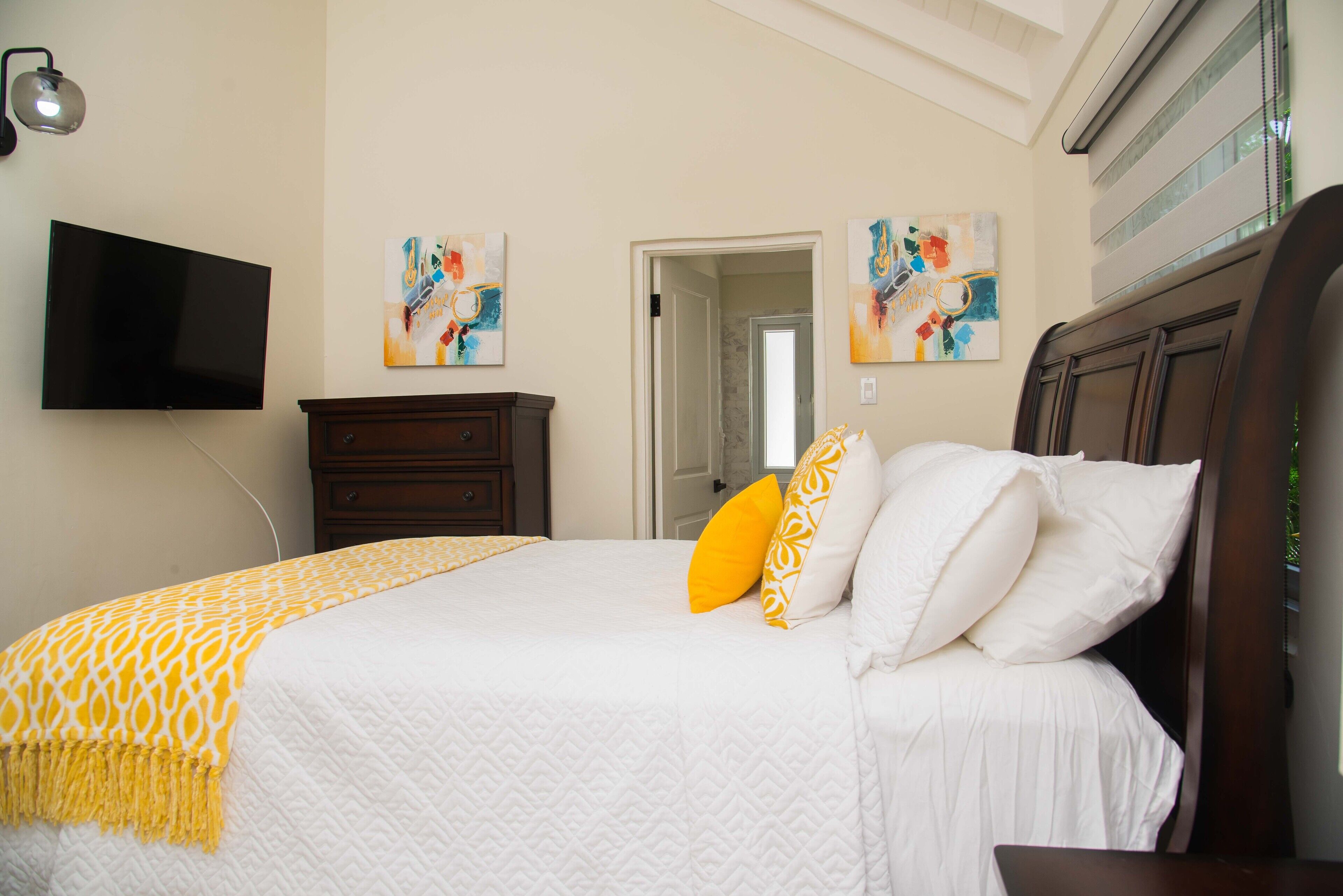 Un dormitorio con cama, televisor de pantalla plana, cómoda de madera y pinturas abstractas en las paredes.