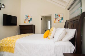 A bedroom with a bed, a flat-screen TV, a wooden dresser, and abstract paintings on the walls. - Modern Villa with private backyard pool (Drax hall)