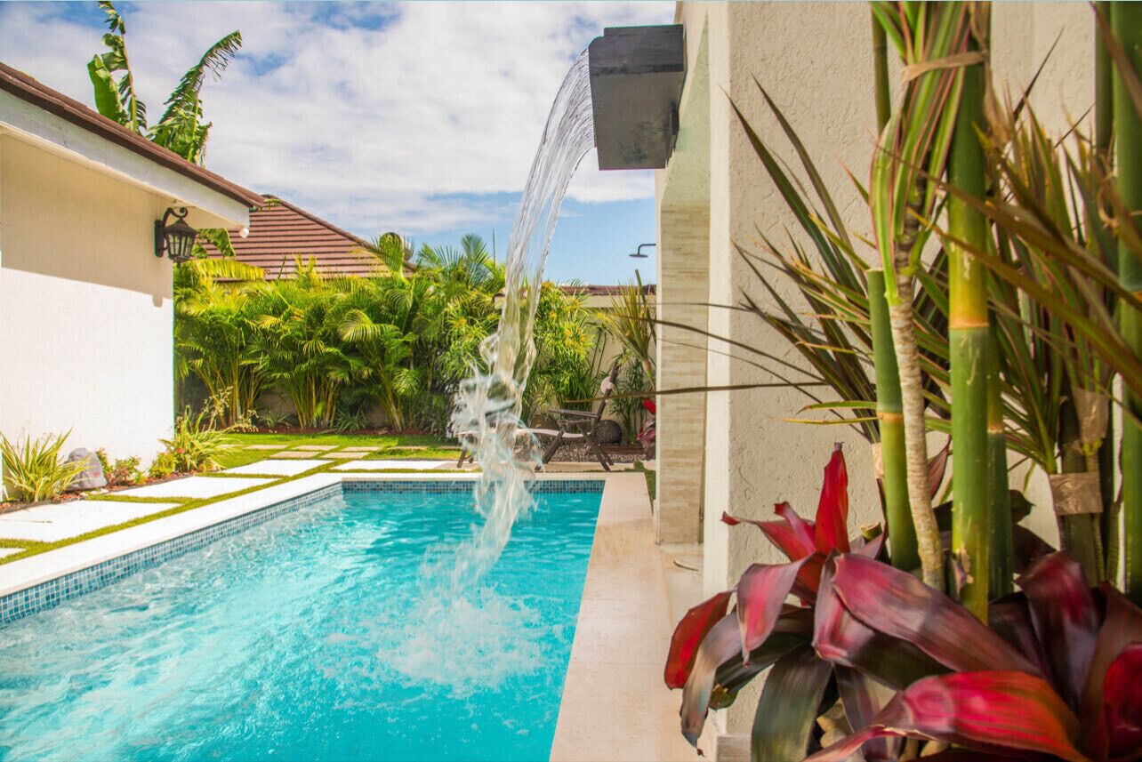 Una piscina con fuente acuática, rodeada de abundante vegetación y un cielo despejado.