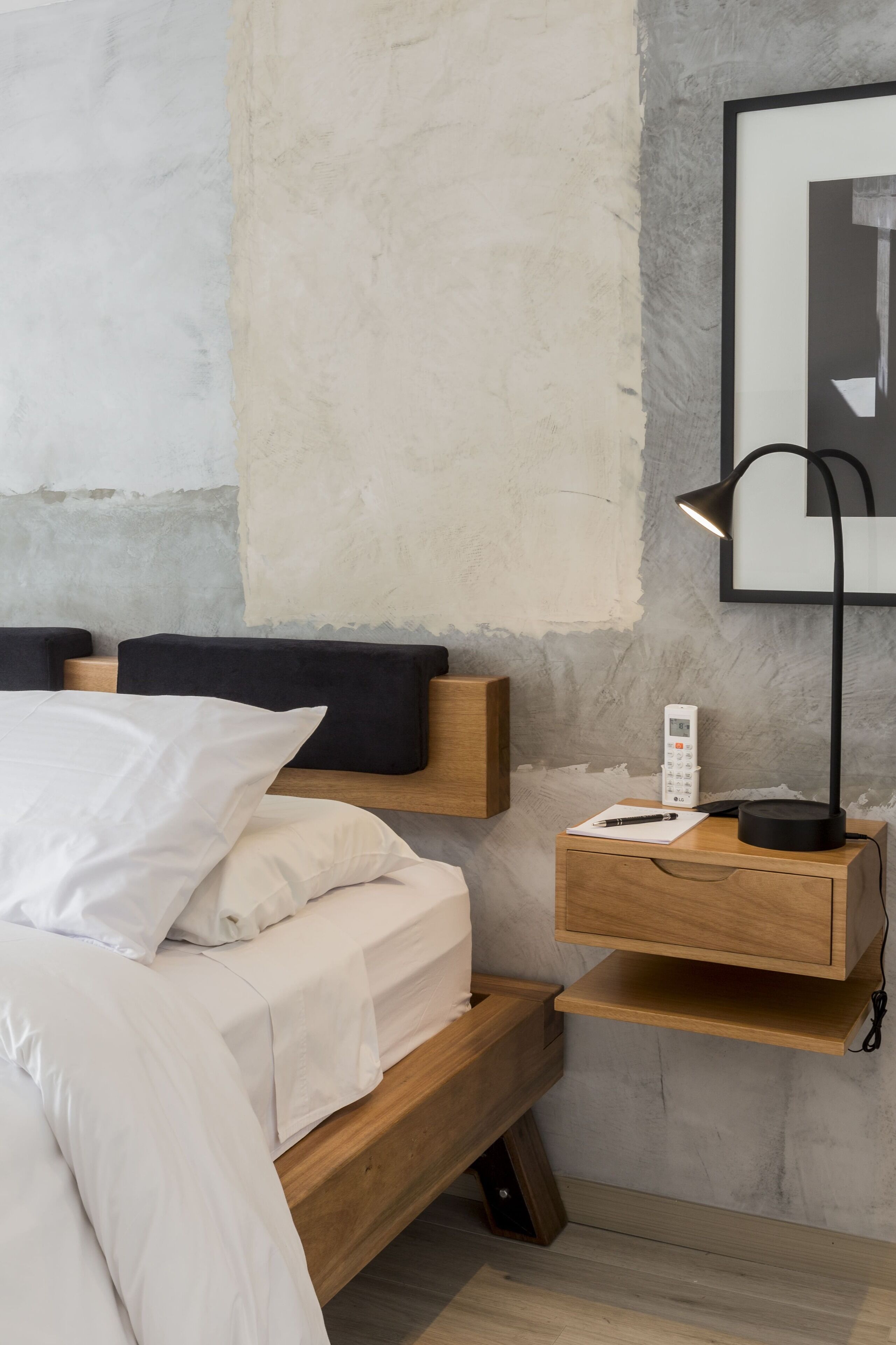 Un dormitorio con cama de madera, ropa de cama blanca, una mesita de noche con lámpara y teléfono.