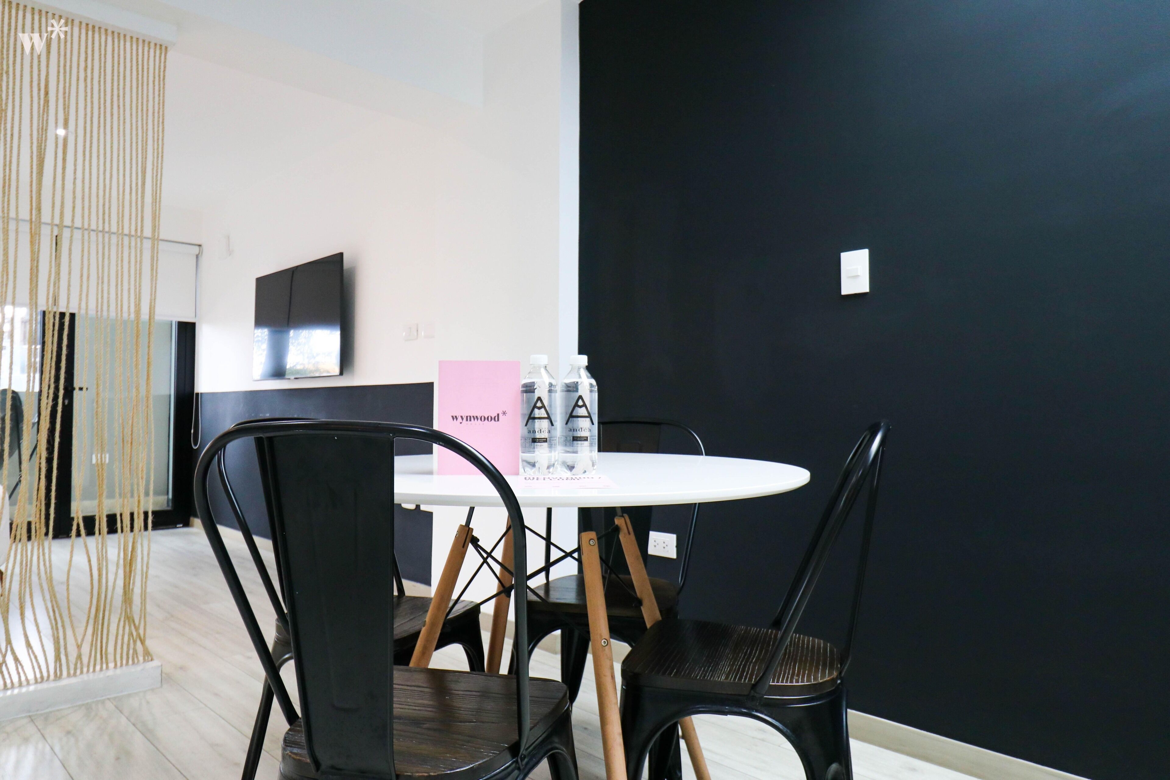 A modern room with a round table, black chairs, a pink sign, and a TV on the wall.