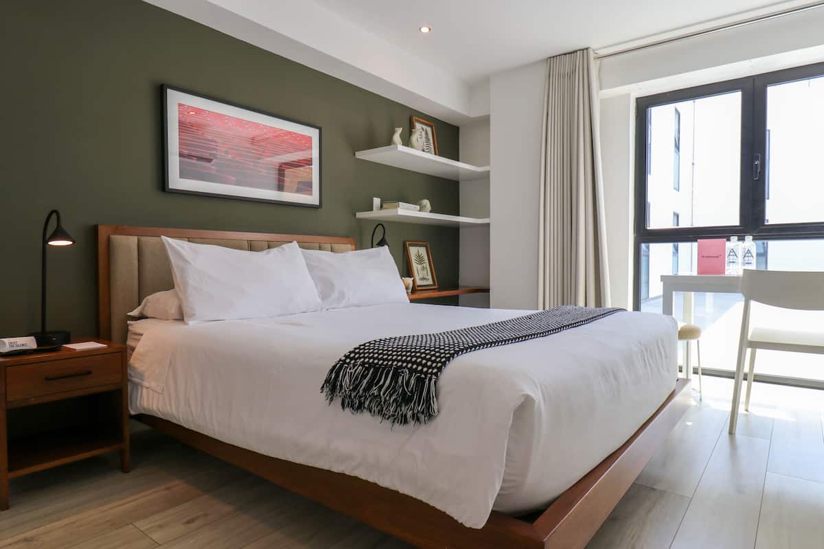 A neatly made bed with white linens, a bedside lamp, and a framed picture on the wall.