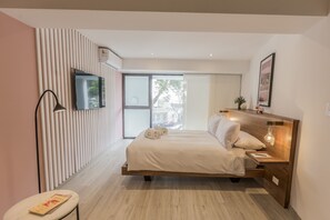A modern bedroom with a large bed, a TV mounted on the wall, and a sliding glass door leading to an outdoor area.
