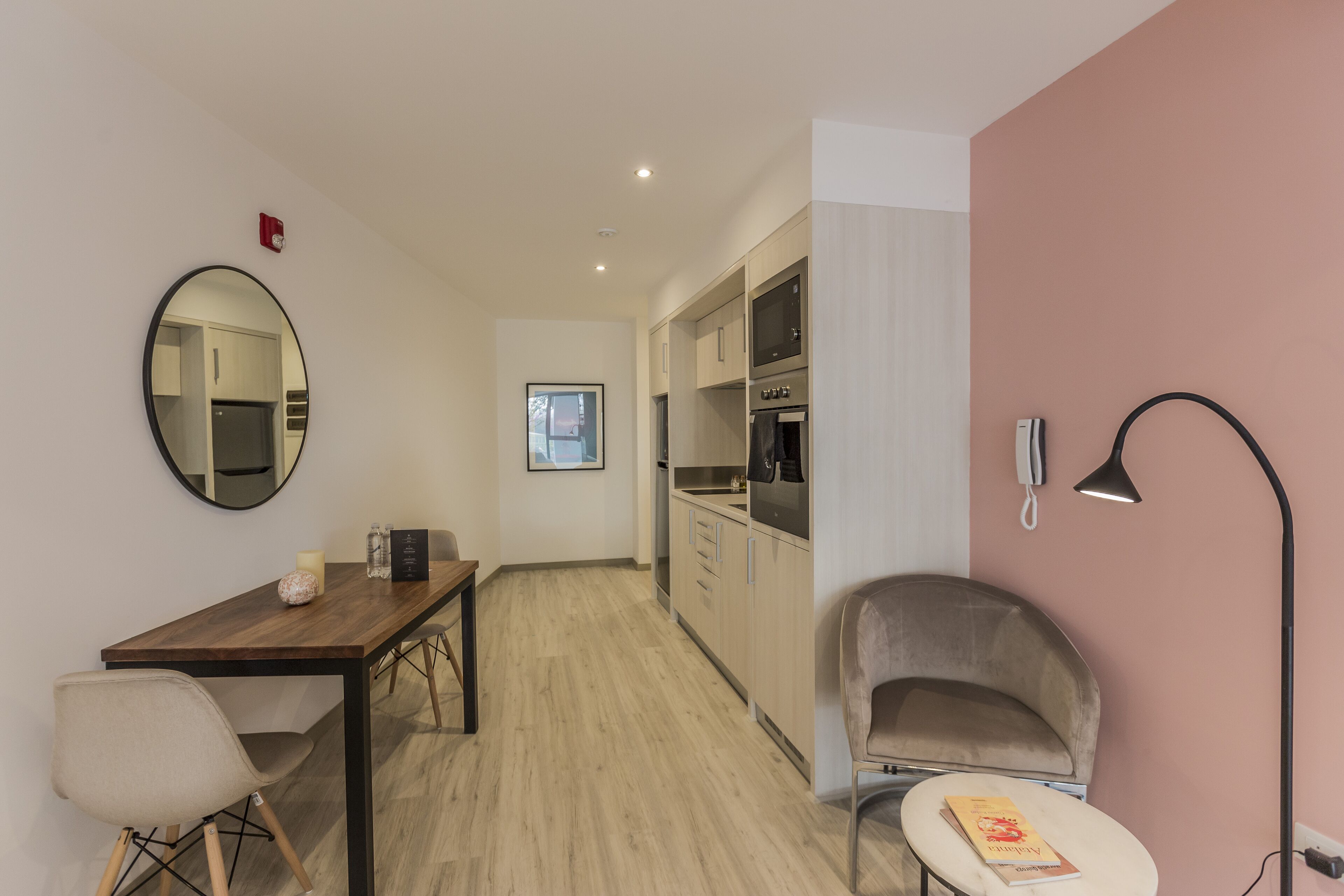 A modern kitchen with built-in appliances, a dining area with a wooden table and chairs, and a cozy reading nook with a chair and a book.