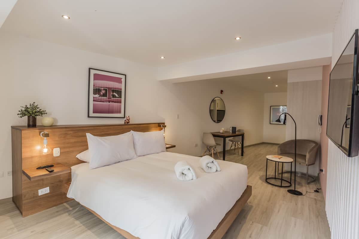 A modern hotel room with a large bed, bedside tables, a desk, and a television.