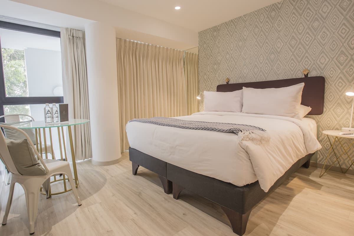 A modern hotel room with a large bed, a glass table, and a chair.