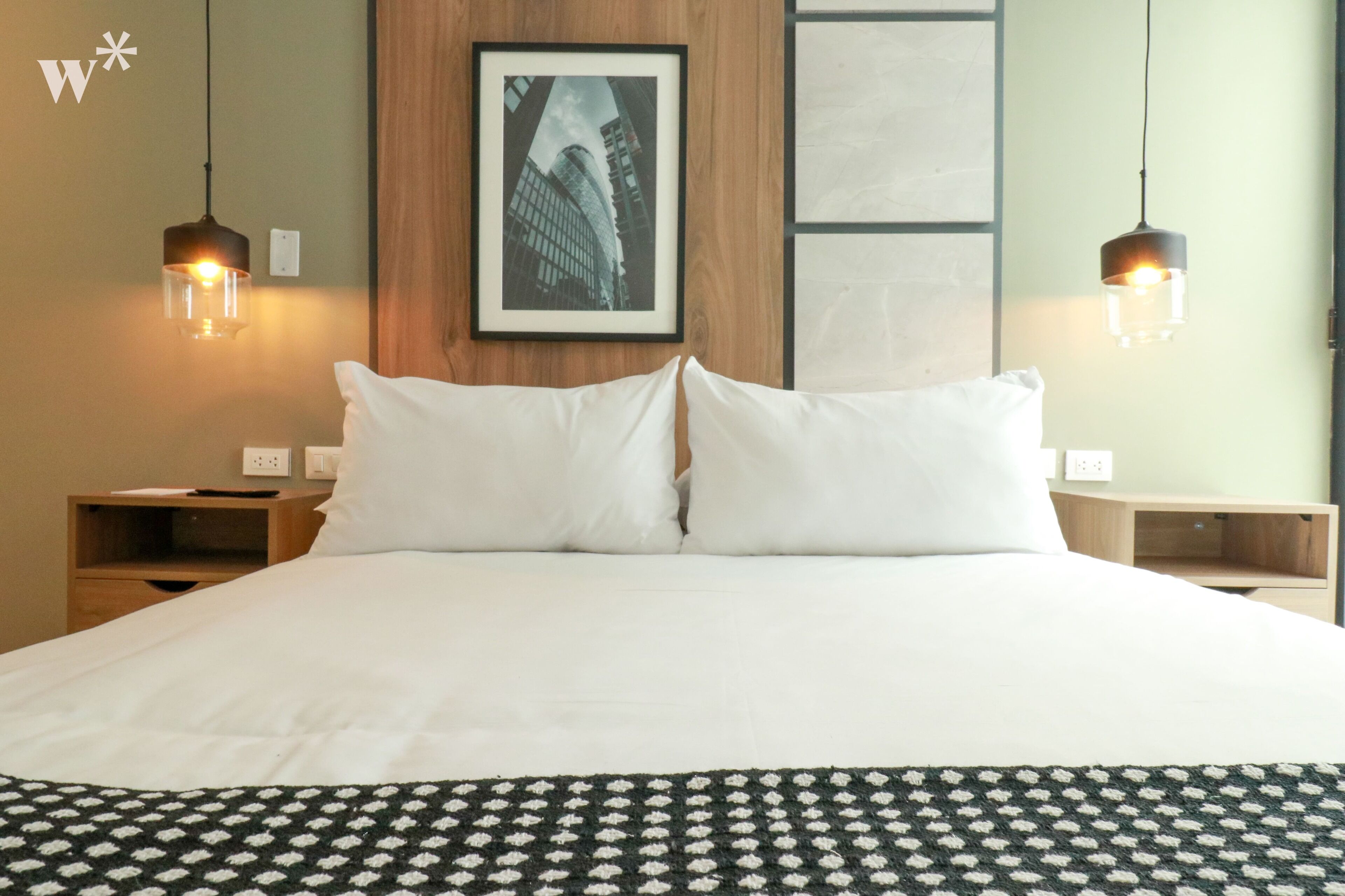 A hotel room with a large bed, two bedside tables, a framed picture on the wall, and two pendant lights.
