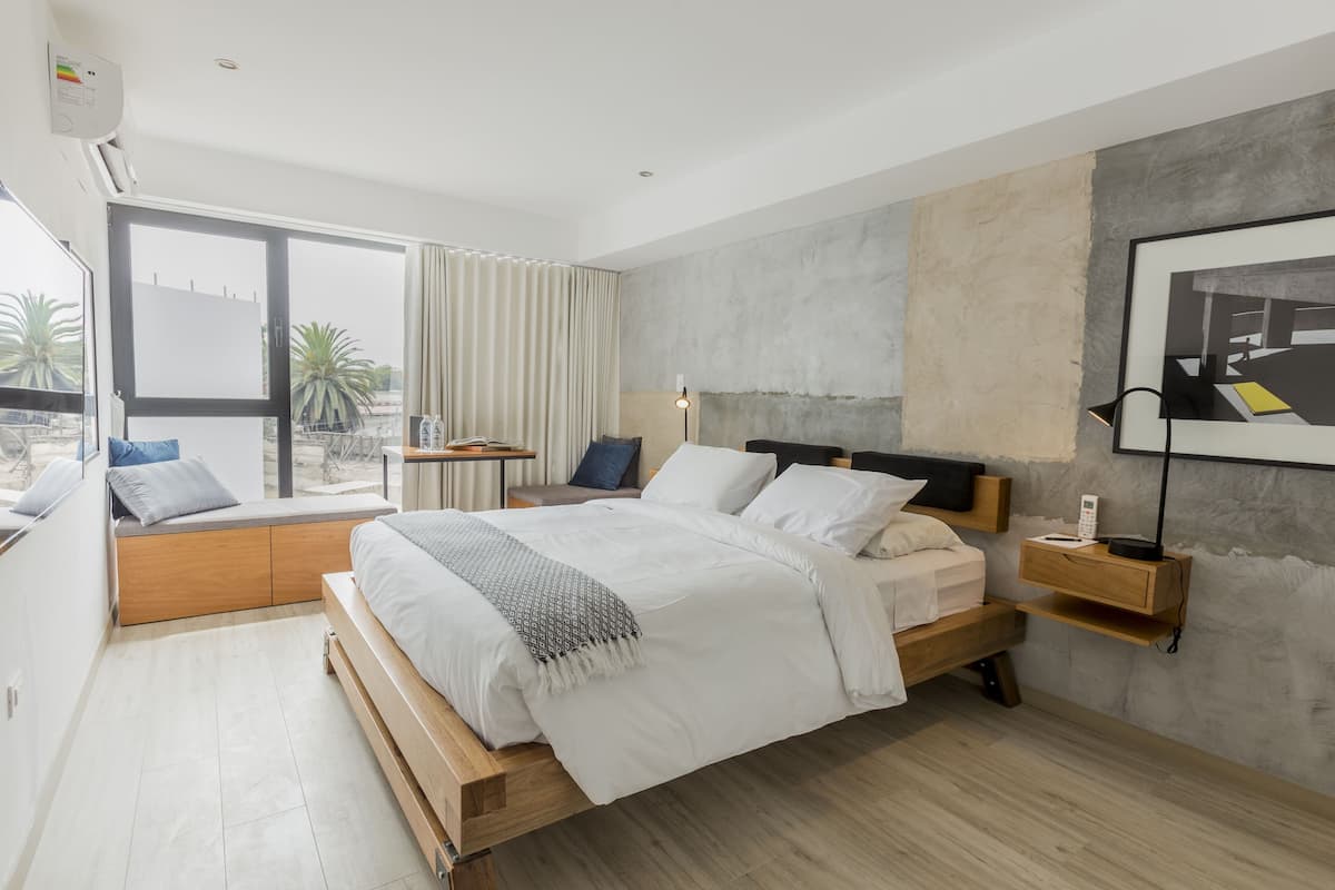 A modern bedroom with a wooden bed, a bedside table, a nightstand, and a large window with curtains.