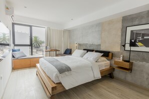 A modern bedroom with a wooden bed, a bedside table, a nightstand, and a large window with curtains. - Primera Parada Lofts by Wynwood-House (Lima)