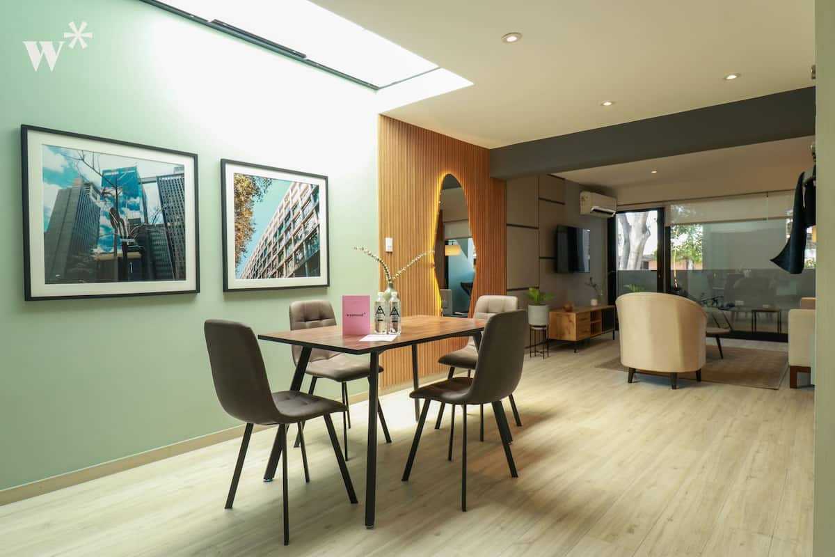 A modern dining area with a wooden table and four chairs, framed cityscape pictures on the wall, and a view through a glass door to an outdoor area.