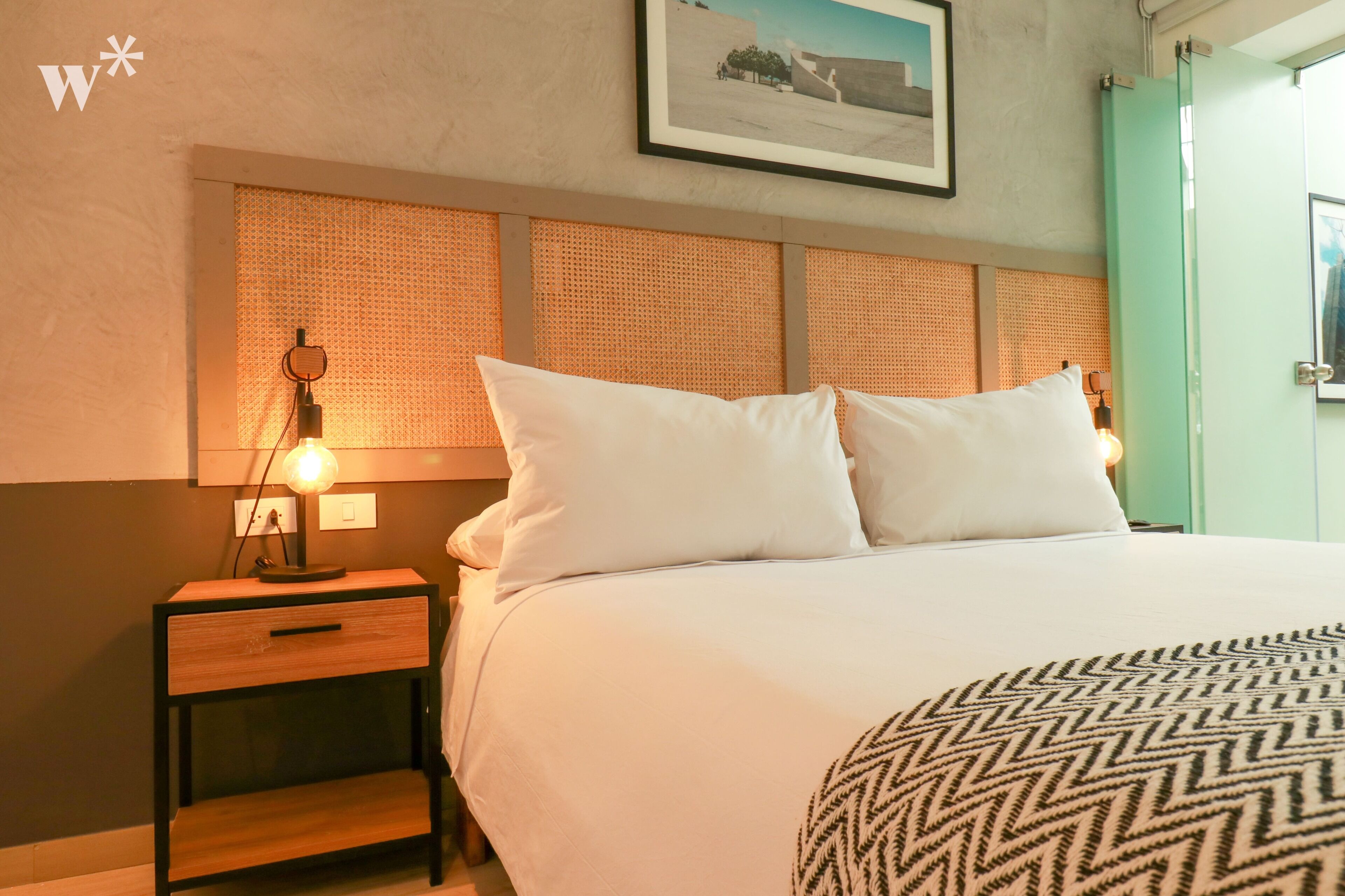 Une chambre d’hôtel avec un lit, une table de chevet, une lampe et un tableau encadré au mur.
