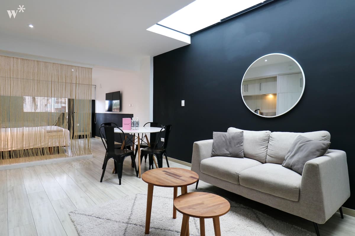 A modern living room with a sofa, two wooden side tables, a round mirror, and a dining area with chairs and a table.