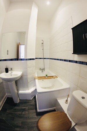 A bathroom with a sink, toilet, bathtub, and a wooden toilet seat. - Lovely Studio Apartment in the Heart of Nottingham (Nottingham)