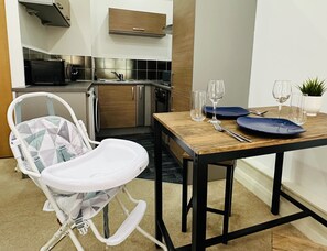 A dining area with a wooden table set for two, a baby high chair, and a kitchen in the background. - Lovely Studio Apartment in the Heart of Nottingham (Nottingham)