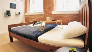 A bedroom with a wooden bed, a small round table, and a brick wall. - Lovely Studio Apartment in the Heart of Nottingham (Nottingham)