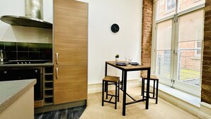 A compact kitchen with a modern stove, wooden cabinets, and a dining area with stools. - Lovely Studio Apartment in the Heart of Nottingham (Nottingham)
