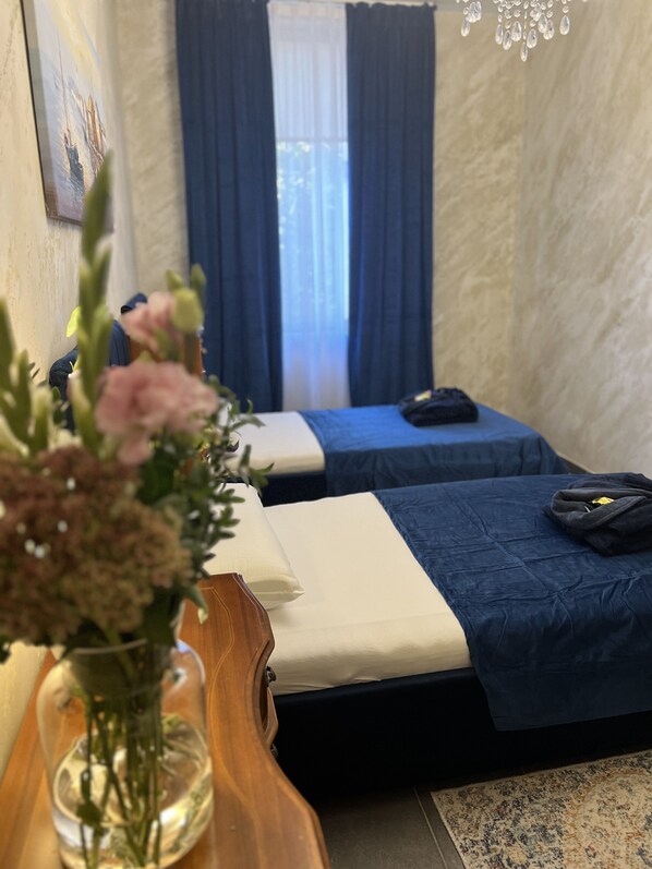 A hotel room with two beds, a wooden desk, a vase with flowers, and a window with curtains.