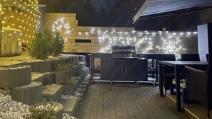 Una terrazza esterna con una griglia per barbecue, zona salotto e luci decorative.