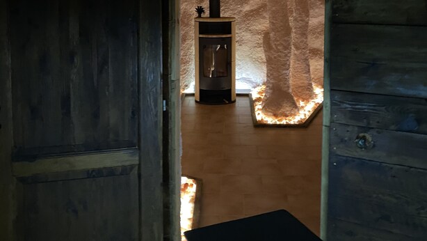 Un interno rustico con una parete in pietra, una porta in legno e un piccolo camino con canna fumaria.