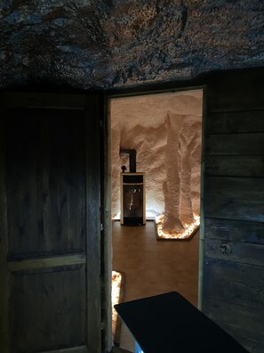 A rustic interior with a stone wall, a wooden door, and a small fireplace with a chimney.