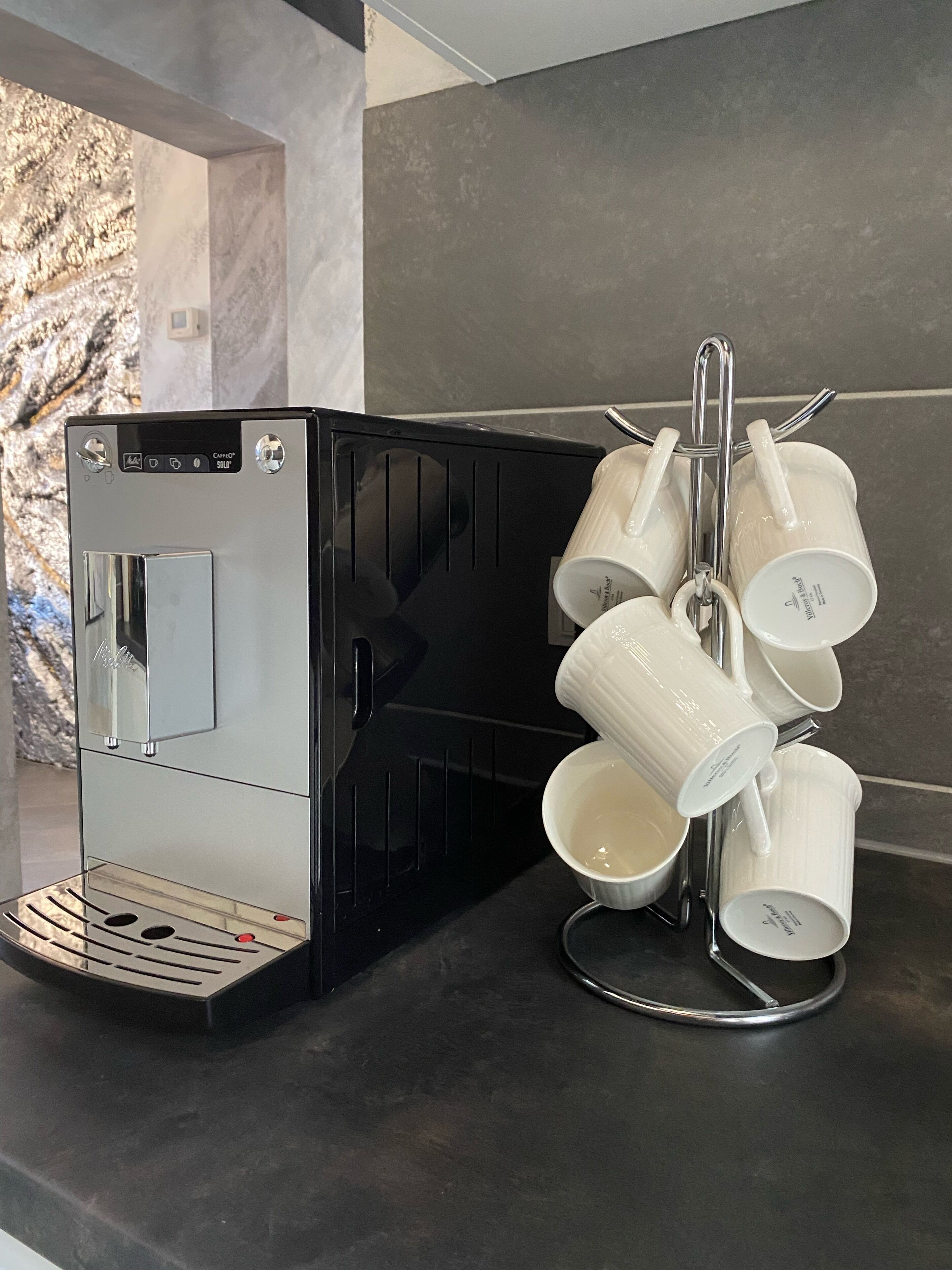 A coffee machine with a milk frother and a mug holder with multiple white mugs.