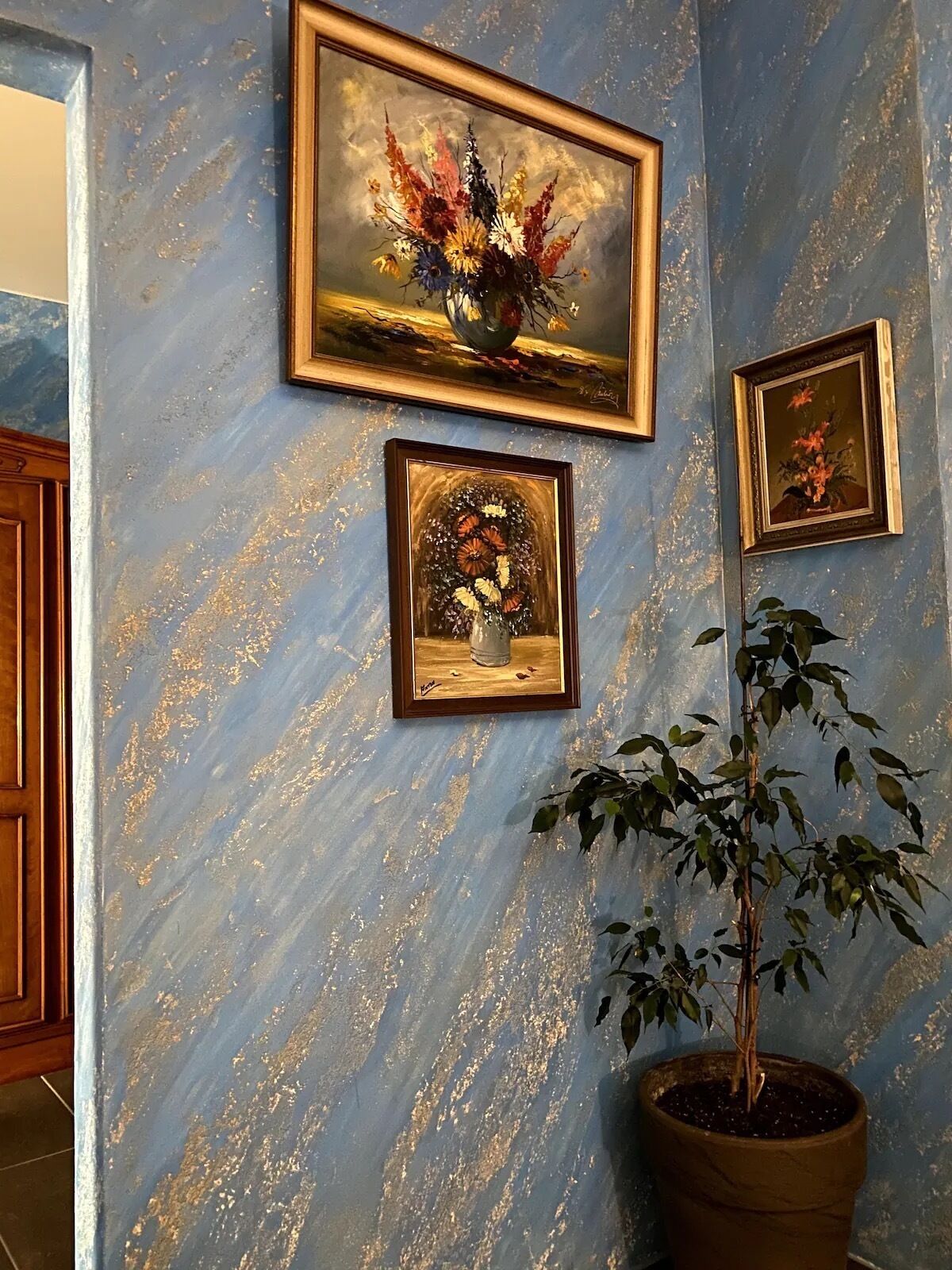 A wall with three framed floral paintings and a potted plant.
