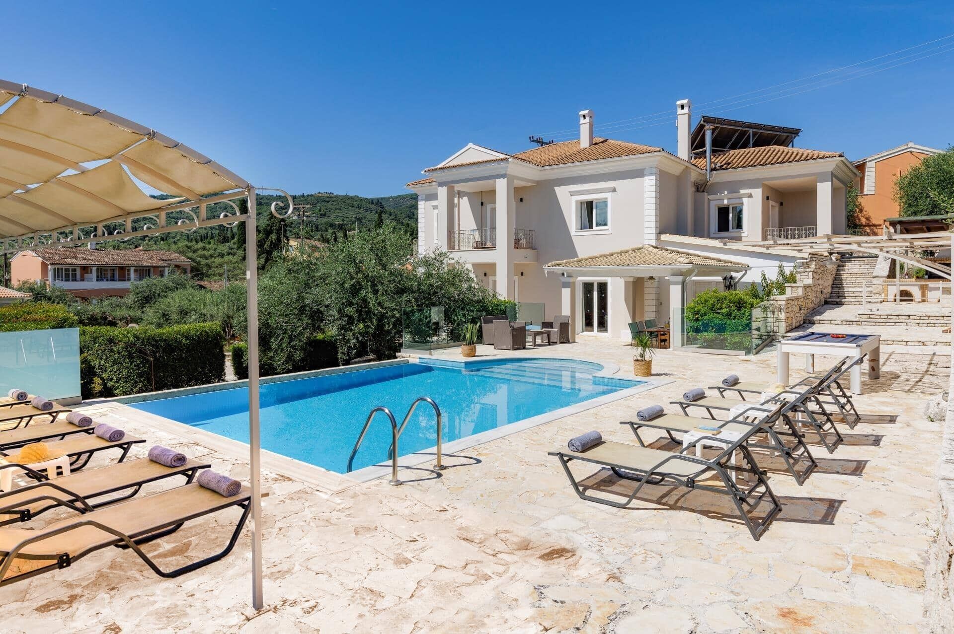 A pool area with lounge chairs, a clear blue pool, and a building with a tiled roof.