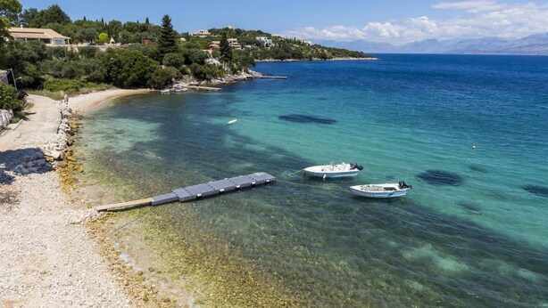 A coastal scene with clear waters, a sandy beach, and boats. - Villa Perla by Villa Plus (Kassiopi)