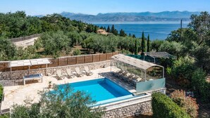 A pool area with lounge chairs, a stone wall, and a view of the sea and mountains. - Villa Perla by Villa Plus (Kassiopi)