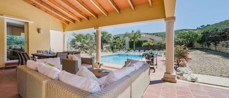 Relax in a serene outdoor space with a wicker sofa and pool views.