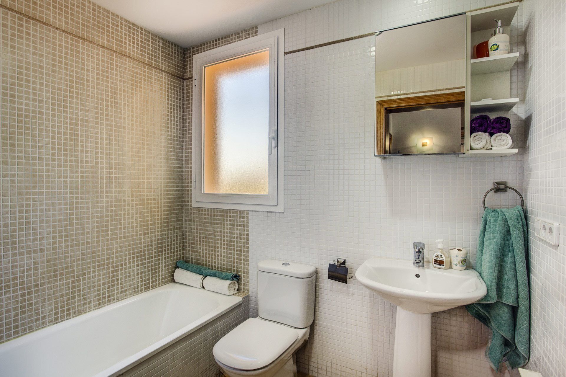 A bathroom with a bathtub, toilet, sink, and a window with frosted glass.