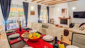 A living room with a dining area, wooden beams, a fireplace, and a pool view. - Villa Magdalena Blanca by Villa Plus (Jávea)