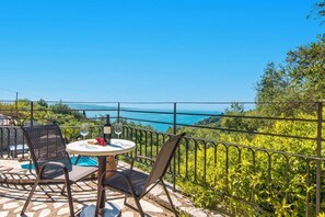 A terrace with a table, chairs, and a view of the sea. - Villa Adonis by Villa Plus (Ionian Islands)