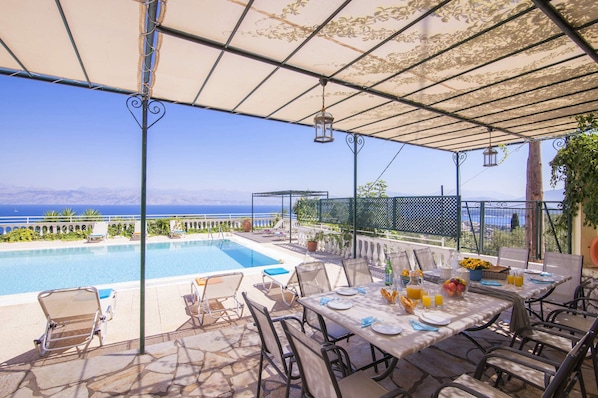 A poolside area with a table set for dining, overlooking a clear blue sea.