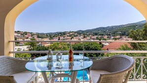 En balkon med et glasbord og fletstole, der giver udsigt over en by med røde tage og et bakket landskab.