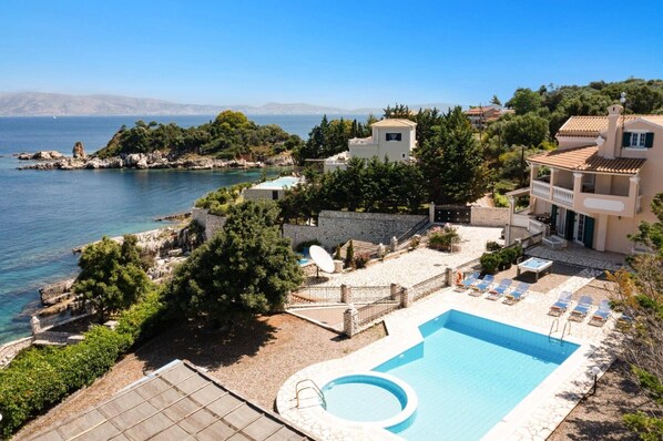 A coastal hotel with a swimming pool, lounge chairs, and a view of the sea.