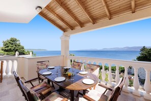 A covered outdoor dining area with a table set for four, overlooking a body of water and distant hills.