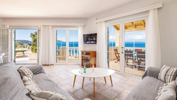 Ein Wohnzimmer mit Sofa, Couchtisch und Fernseher. Es gibt einen Balkon mit Blick aufs Meer.