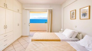Ein Hotelzimmer mit zwei Betten, einem Schrank, einem Balkon mit Meerblick und zwei gerahmten Bildern an der Wand.