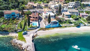 An aerial view of a coastal residential area with houses, a swimming pool, and a dock. - Villa Annie by Villa Plus (Imerolia)