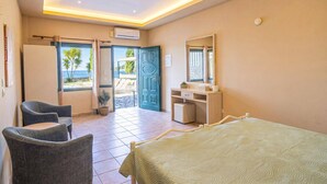 A hotel room with a bed, a desk, a chair, a bathroom, and a view of the sea. - Villa Annie by Villa Plus (Imerolia)