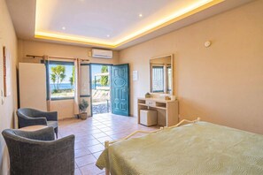 A hotel room with a bed, a desk, a chair, a bathroom, and a view of the sea.