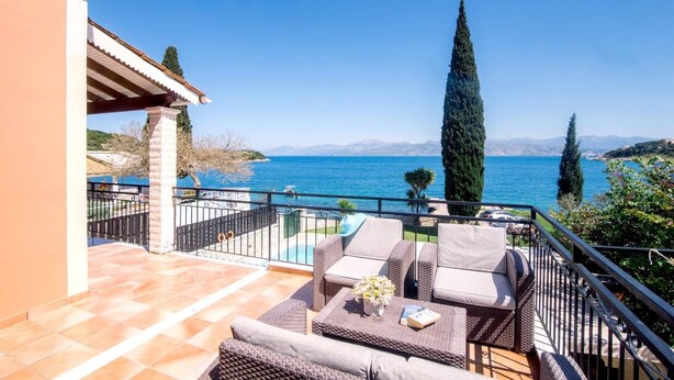 A balcony with outdoor furniture, a view of the sea, and a tall cypress tree. - Villa Annie by Villa Plus (Imerolia)