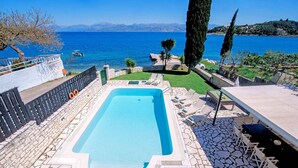 A swimming pool with a stone deck, lounge chairs, and a view of the sea. - Villa Annie by Villa Plus (Imerolia)